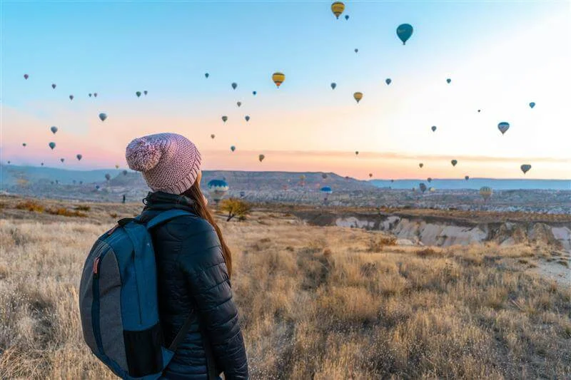 Person in pink hat with hot air balloons in the sky